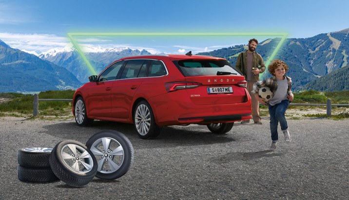 Roter Skoda Octavia vor einer Bergkulisse und ein Kind spielt mit einem Fußball und der Vater sieht ihm zu.